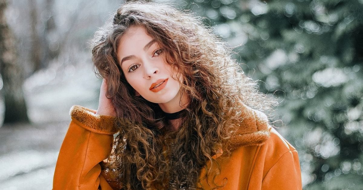 A woman with curly hair wearing an orange jacket, embodying the elegance of old money hairstyles in a seasonal setting.