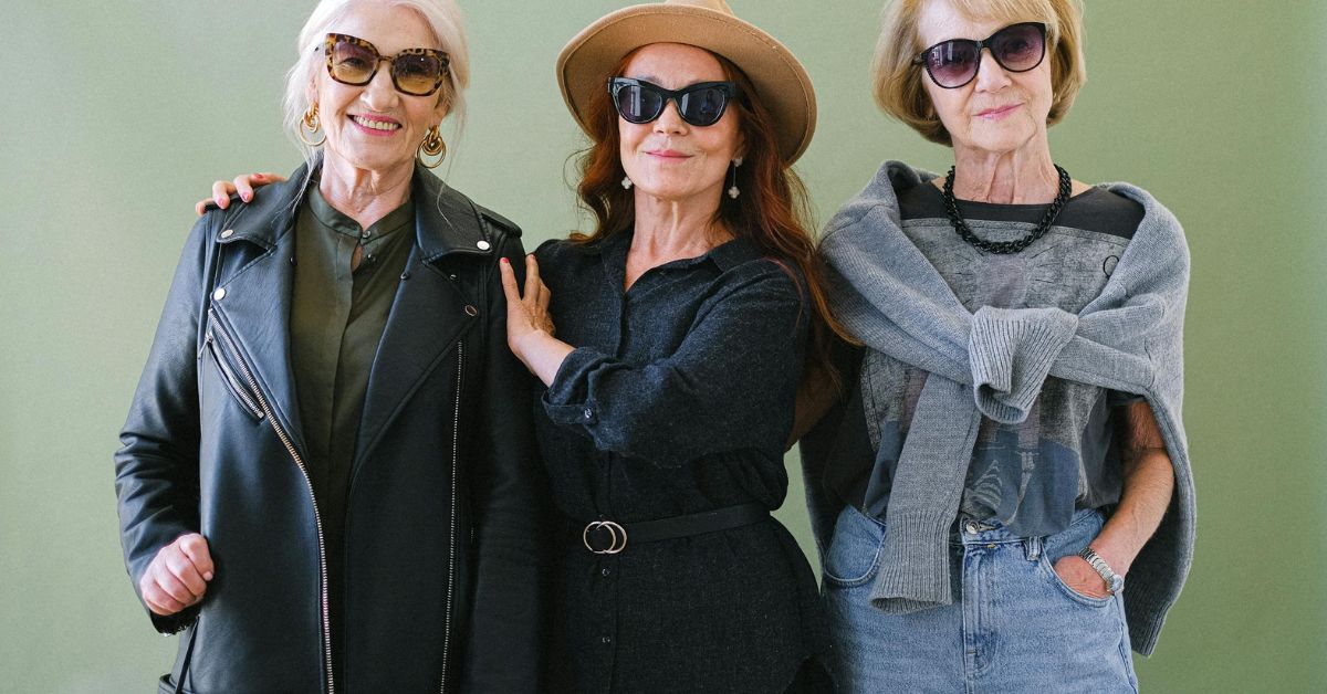 Three women in sunglasses and jackets pose stylishly, showcasing Old Money fashion elegance in a chic outdoor setting.