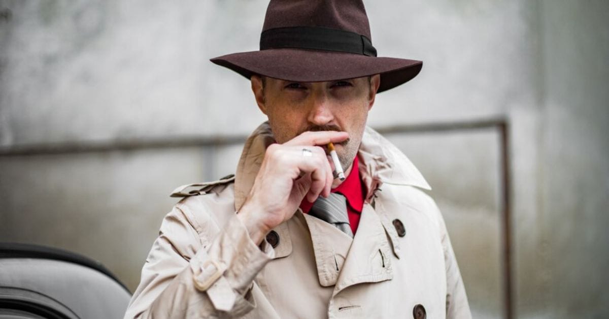 A man in a trench coat and hat, embodying old money style, smokes a cigarette with an air of elegance and sophistication.
