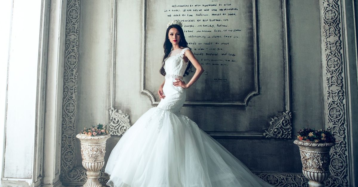 A woman in a vintage wedding dress poses gracefully in front of a textured wall, embodying old money elegance.