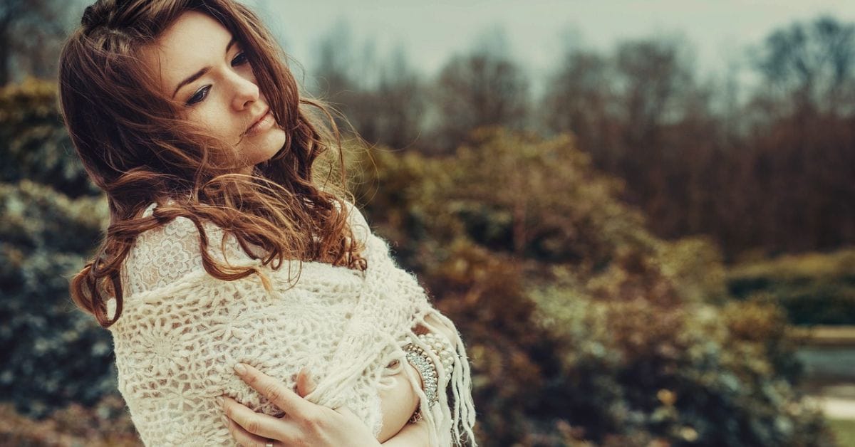 A woman in a white sweater stands gracefully in the grass, embodying the elegance of old money aesthetics in her hairstyle.