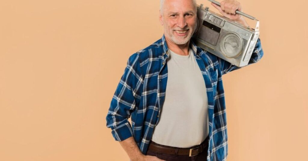 An older man in classic attire smiles while holding a vintage radio, embodying timeless elegance and charm