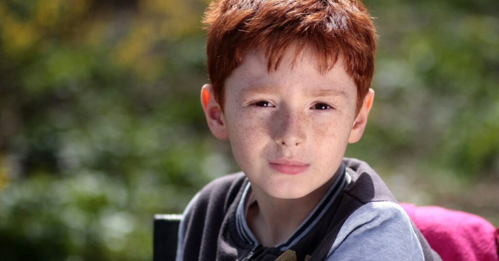 A young boy with freckles sits on a bench, embodying the charm of Old Money Edgar style.