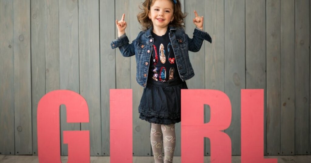 A little girl stands proudly in front of a sign that reads "girl," names showcasing her playful spirit and charm.