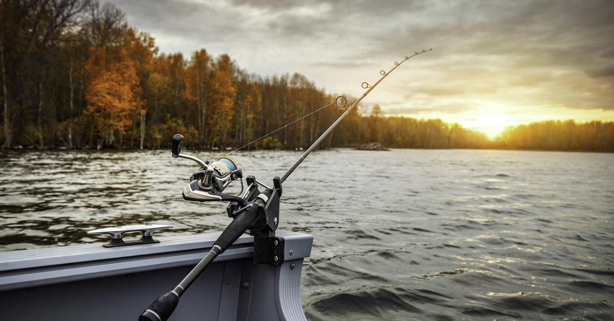 A fishing rod and reel resting on a boat, silhouetted against a vibrant sunset sky.